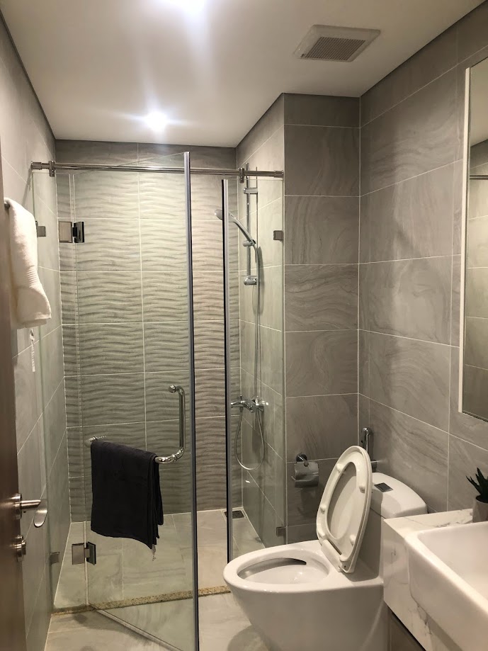 Phòng tắm hiện đại với buồng tắm kính, vòi sen treo tường, bồn cầu và lavabo đá màu xám sáng